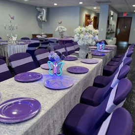 Long banquet tables with purple plates, butterfly centerpieces, and purple chair covers set up for an event.