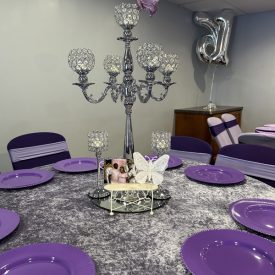 Round table with purple plates, crystal candelabra centerpiece, butterfly decor, and a silver “31” balloon in background.
