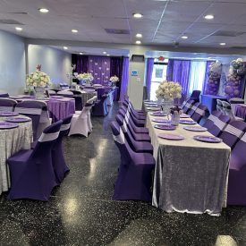 Room set for an event with purple and silver decor, covered tables and chairs, and floral centerpieces.