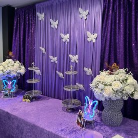 Decorated purple dessert table with tiered trays, white flower arrangements, and butterfly accents.