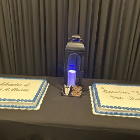 Two sheet cakes with blue trim and a lantern are displayed on a table with a black tablecloth and backdrop.