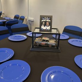 A table with blue plates, a model car in a glass case, and a framed photo as the centerpiece.