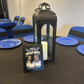 A black lantern and a framed memorial photo are on a table set with blue plates and black tablecloth.